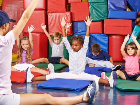 Children sitting in front of a coach stretching on gymnastics tumbling mats