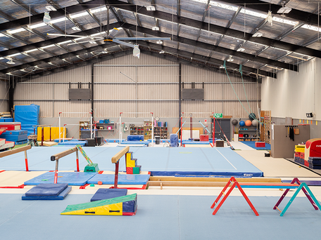 View of entire gym floor, filled with bars, vaults & tumbling mats