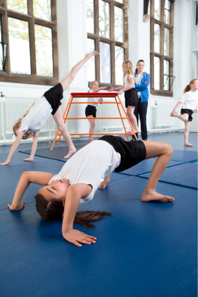 School kids in gymnastics bridges, as the coach oversees them