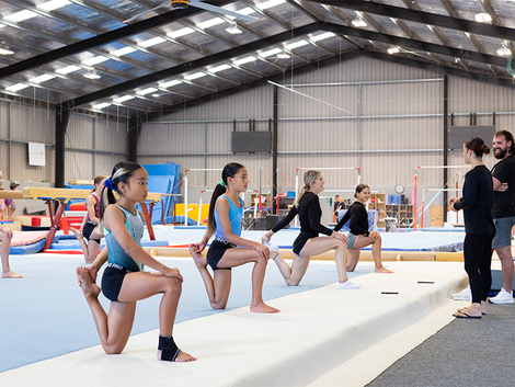 Young gymnasts lined up in a synchronised stretch, while the coaches oversee